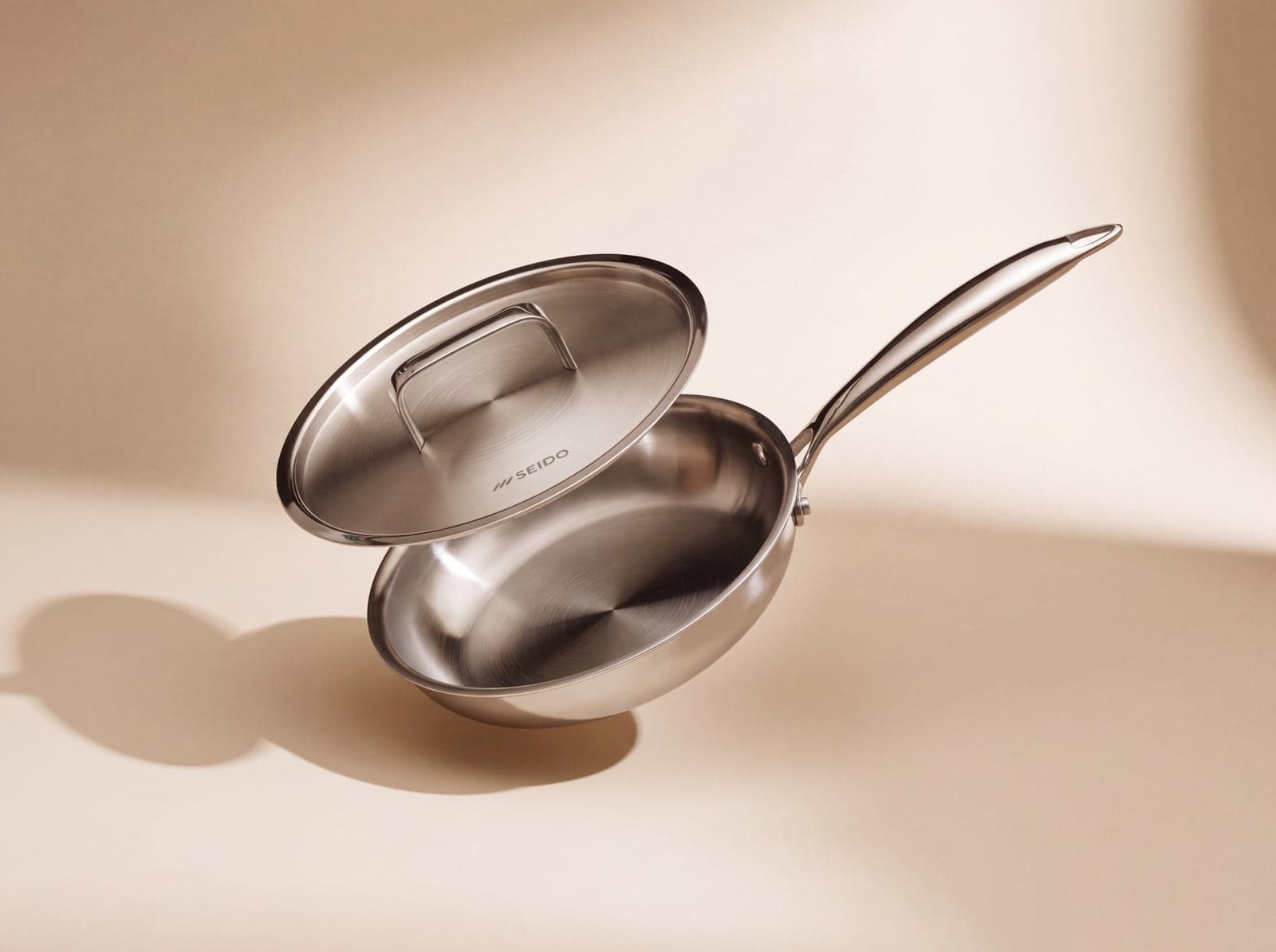 SEIDO 20 cm stainless steel frying pan with its lid, on a soft beige background