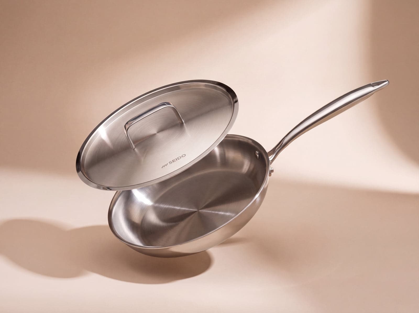 SEIDO Sear Series 24 cm stainless steel frying pan with lid, floating on a soft beige background