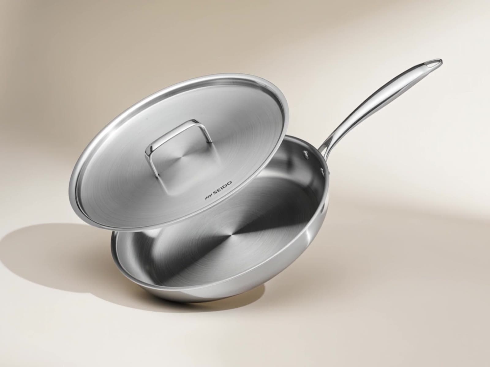 SEIDO stainless steel frying pan with its matching lid on a cream background
