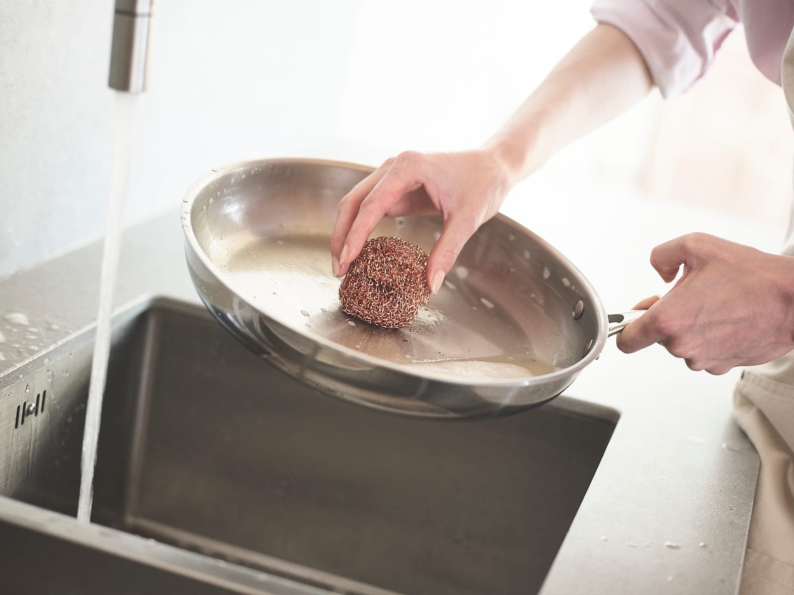 Washing a stainless steel frying pan by hand under a running tap
